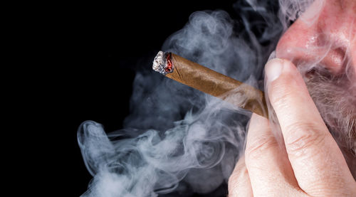 Man smoking cigar against black background