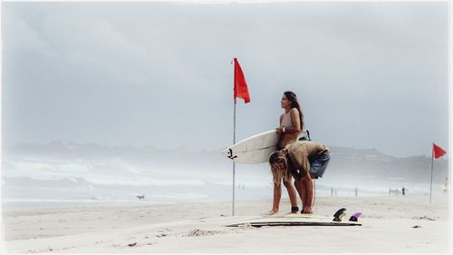 Full length of surfers on beach against sky