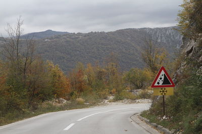 Road sign by trees against sky