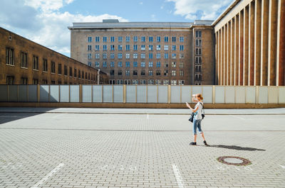 Full length side view of woman photographing on street against buildings