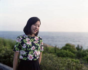 Smiling woman standing at sea shore against clear sky