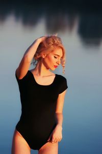 Young woman with hand in hair standing against lake during sunset