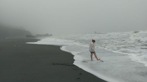Woman standing at beach against foggy sky during stormy weather