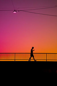 Silhouette man standing on bridge against sky during sunset