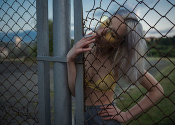 Woman smoking cigarette at chainlink fence