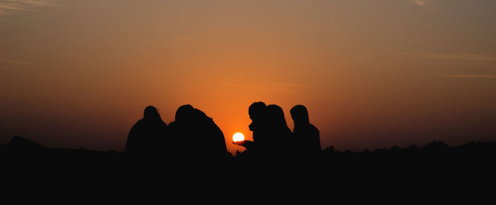 Silhouette friends on field against sky during sunrise