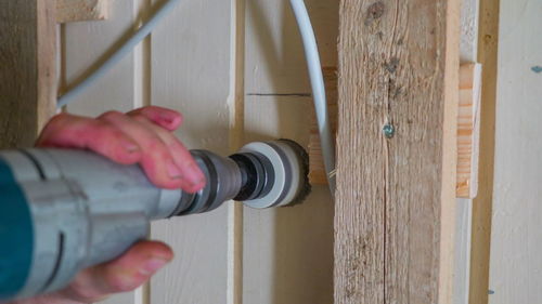 Cropped hand using drilling tool on wooden wall