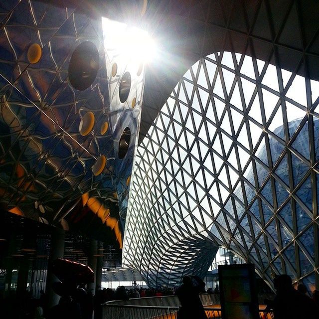 architecture, built structure, low angle view, indoors, sunlight, sunbeam, ceiling, sun, glass - material, lens flare, modern, building exterior, pattern, silhouette, architectural feature, shadow, window, day, building, incidental people