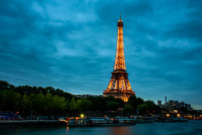 Illuminated eiffel tower by river against sky