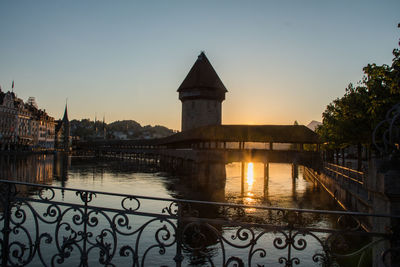 Bridge over river by buildings against sky during sunset