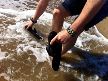Low section of man cleaning shoes in water in sea