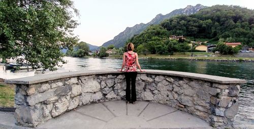 Rear view of woman standing by lake against sky