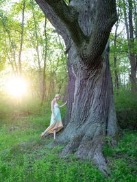 Woman standing by tree trunk in forest