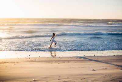 Young woman running at beach against clear sky during sunset