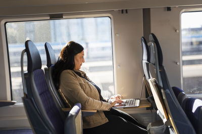 Mid adult woman in train using laptop