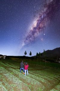 Rear view of friends on field against sky at night
