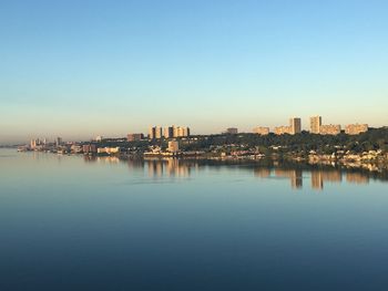 Scenic view of river by buildings against clear blue sky