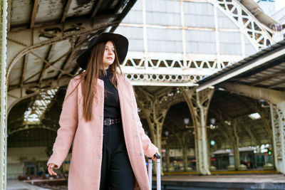 Young woman in coat walks with suitcase along empty platform of railway