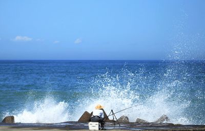 View of man fishing and waves crashing on rocks