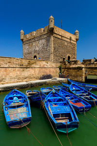 Blue boats moored in canal by castle against clear blue sky during sunny day