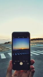 Close-up of hand holding mobile phone at beach against sky