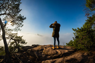 Man standing on rock against blue sky