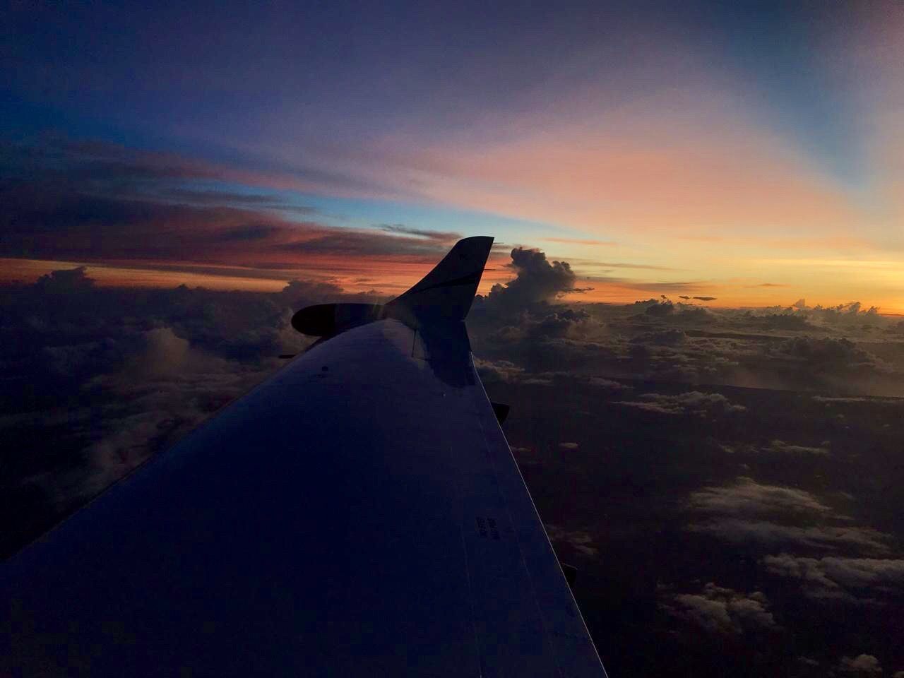 AIRPLANE FLYING OVER LANDSCAPE AGAINST SKY DURING SUNSET