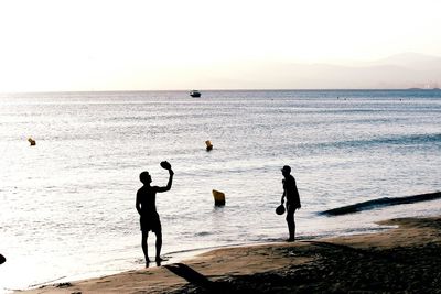 Silhouette people standing on beach against clear sky