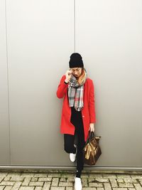 Young woman while standing on footpath against wall