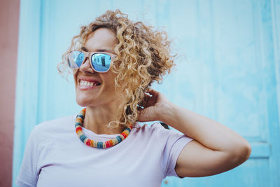 Portrait of young woman wearing sunglasses while standing against blue background