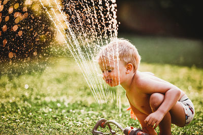 Young boy sticking tongue out drinking water from sprinkler in garden