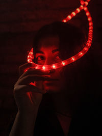 Portrait of woman holding illuminated lighting equipment in darkroom