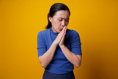 Young woman looking away while standing against yellow background