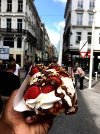 Hand holding ice cream cone on street in city