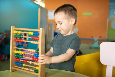 Smiling toddler boy playing with colourful toy abacus in a children's entertainment center.