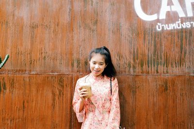 Portrait of smiling girl standing against wooden wall