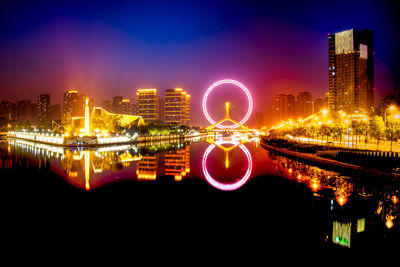 Illuminated city by river against sky at night