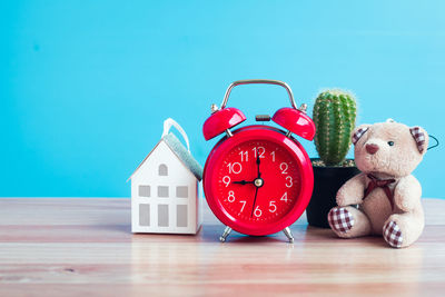 Close-up of clock and model house with teddy bear on table against wall