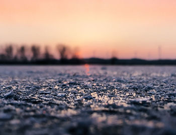 Surface level on lakeshore against orange sky during winter