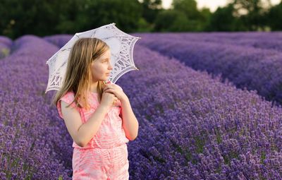 Teenage girl holding umbrella while standing against lavender field