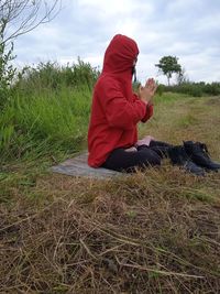 Side view of woman sitting on field against sky