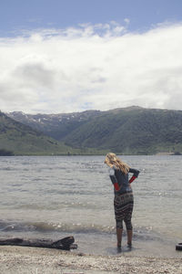 Rear view of woman standing on beach against sky