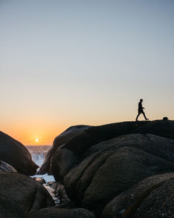 Silhouette man walking on rock against sky during sunset