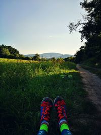 Low section of person wearing red shoe sitting on grass against clear sky