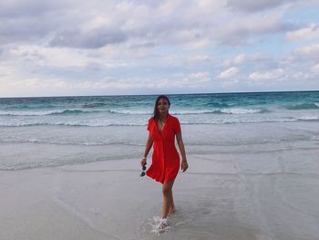 Full length portrait of woman walking at beach against sky