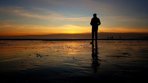 Silhouette of man standing on beach looking into sunset