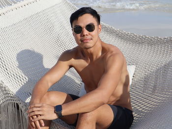 Portrait of young man wearing sunglasses while sitting on pier