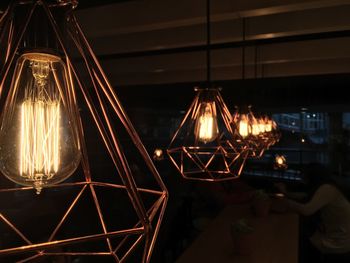Close-up of illuminated light bulbs hanging in row at restaurant during night