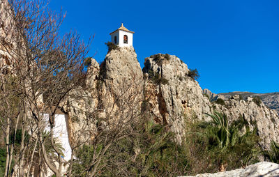 Low angle view of bell tower on rocky mountain at guadalest