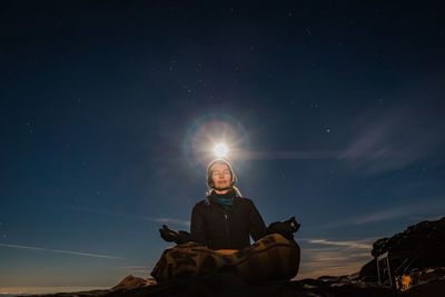 Low angle view of man sitting on rock against sky at night